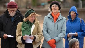 A bunch of singers with winter hats on singing happily on the beach